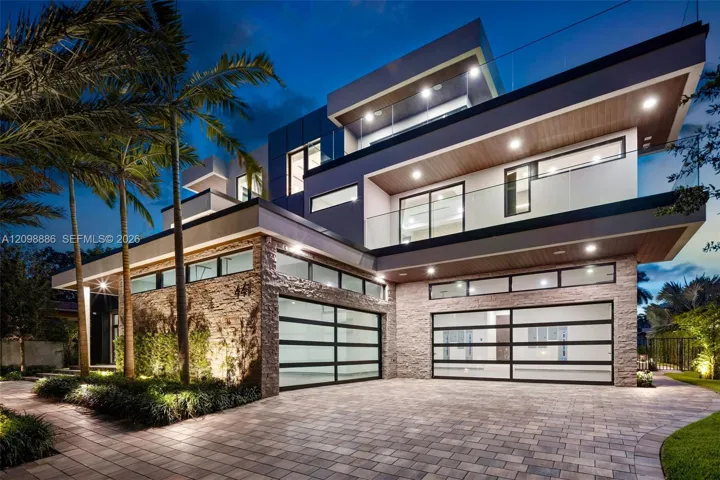 Contemporary multi-level exterior featuring stacked stone masonry, horizontal glass panel garage doors, glass-railed balconies, and wood-finish soffits