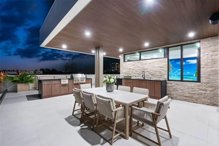Covered outdoor terrace featuring a built-in stainless steel grill, stone veneer accent wall, recessed lighting, and expansive wood-finish ceiling soffits