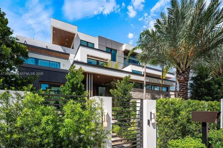 Modern multi-level exterior featuring white stucco facade, dark wood-finish soffits, integrated glass balcony railings, stone cladding accents, and horizontal slat privacy gating