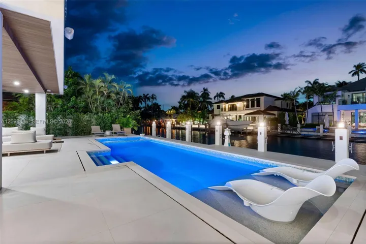 Rectangular swimming pool featuring a tanning ledge and tile surround, set against a waterfront bulkhead with concrete patio and recessed ceiling lighting