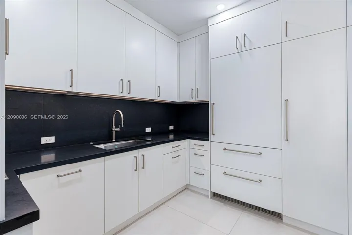 Kitchen featuring flat-panel white cabinetry, contrasting dark stone countertops, integrated panel-ready refrigerator, stainless steel undermount sink with gooseneck faucet, and recessed ceiling lighting