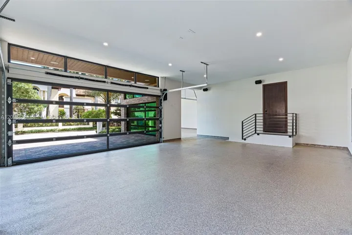 Multi-car garage featuring a full-glass overhead door, speckled epoxy flooring, recessed lighting, and a raised entry platform with a metal railing