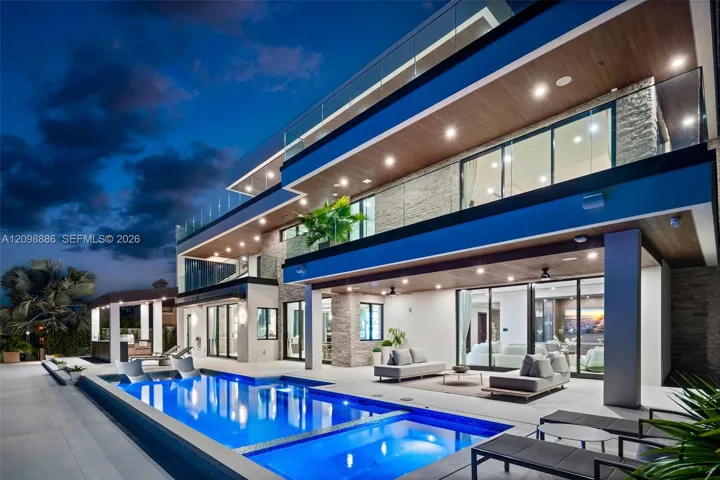 Contemporary multi-level exterior featuring stacked stone masonry, recessed soffit lighting, glass panel balcony railings, and a heated pool with an integrated spa
