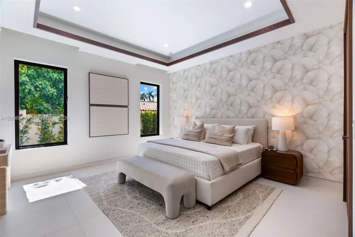 Tray ceiling with dark wood-finish trim, patterned wallpaper accent wall, large picture windows with black frames, and neutral tile flooring