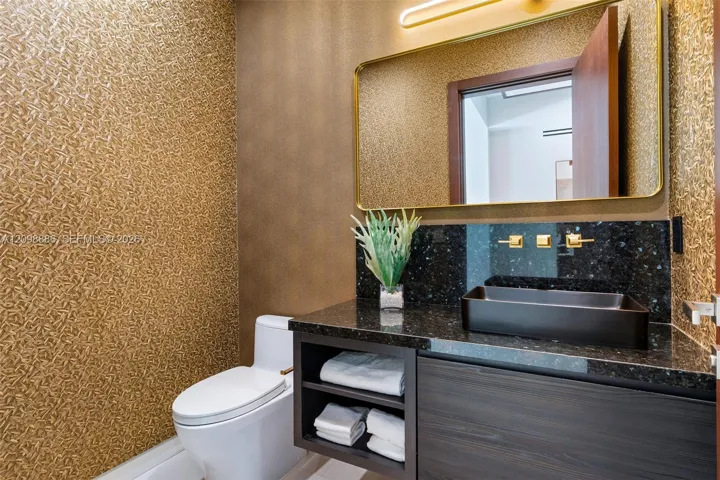 Floating vanity featuring a dark wood-finish, polished stone countertop, and rectangular vessel sink with gold-tone wall-mounted hardware