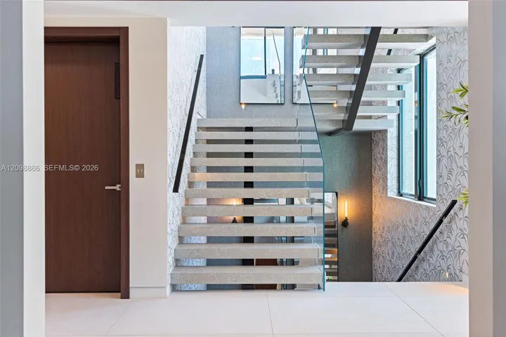 Open-riser staircase featuring terrazzo treads, a glass panel railing, and wall-mounted linear lighting