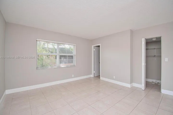 Neutral-toned interior featuring large-format tile flooring, a dual-pane window with adjustable blinds, and a built-in closet with folding doors and wire shelving