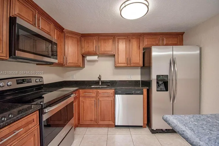 Kitchen featuring wood cabinetry, stone-surface countertops, tile flooring, and stainless steel appliances