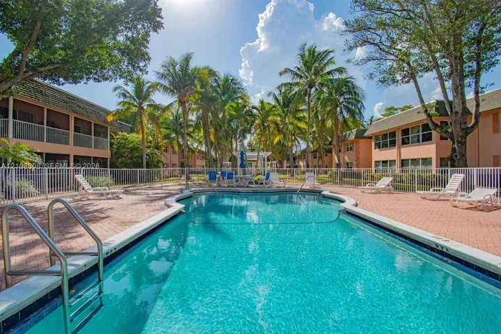 Swimming pool with a paved deck, metal perimeter fencing, and mature palm trees