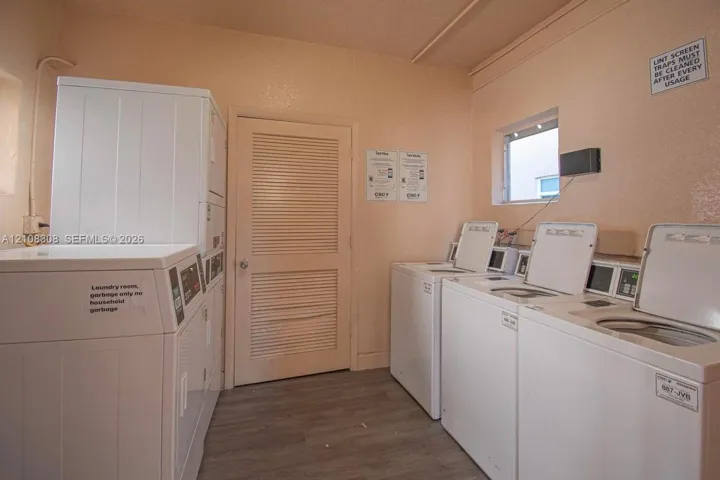 Laundry facility featuring multiple top-load washers, a stackable dryer unit, louvered interior door, and wood-finish flooring