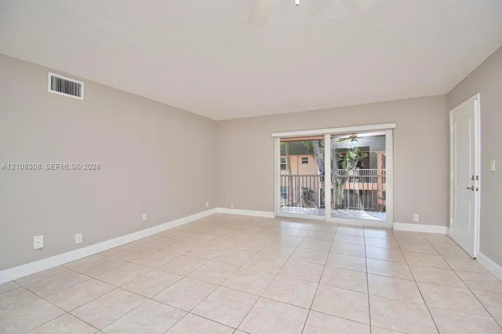 Neutral-toned interior space featuring ceramic tile flooring, sliding glass patio doors, and a ceiling-mounted fan
