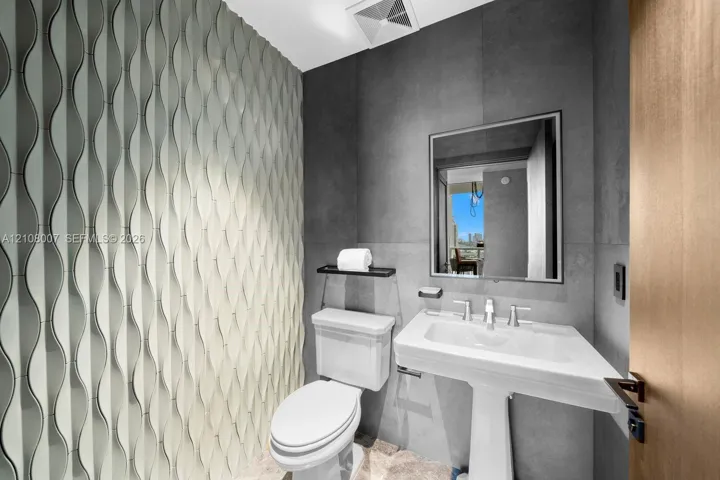 Textured dimensional wall tile, matte charcoal large-format wall surfacing, pedestal sink with polished chrome hardware, and wood-finish door