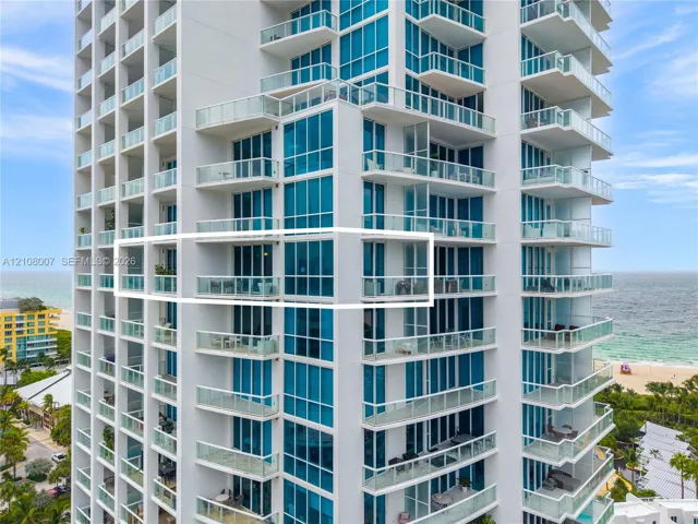 High-rise residential tower featuring floor-to-ceiling blue glass curtain walls, wrap-around private balconies with glass railings, and direct coastal proximity