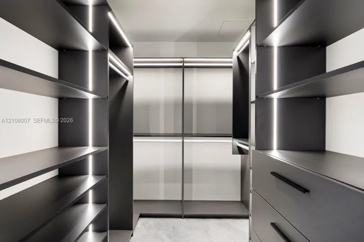 Custom walk-in closet featuring matte charcoal cabinetry, integrated vertical LED accent lighting, open shelving, integrated garment rods, and deep-drawer storage with matte black hardware