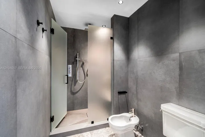 Full-height charcoal large-format wall tiling, walk-in shower with a frosted glass partition, handheld shower fixture, and wall-mounted robe hooks