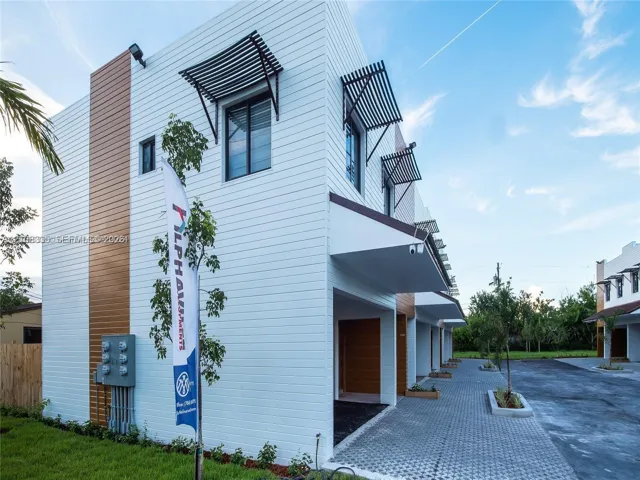 Modern exterior featuring horizontal white lap siding, vertical wood-finish paneling, custom metal window awnings, and a paver driveway