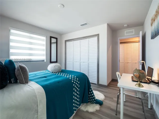 Bedroom featuring wood-finish flooring, louvered-style closet doors, and horizontal-banded window shades