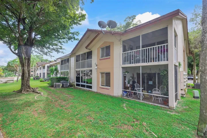 Multi-story exterior featuring a light-colored stucco facade, two-level screened-in lanais, and mature shade trees