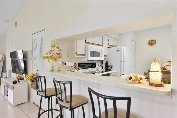 Kitchen featuring a breakfast bar with a solid surface countertop, white cabinetry, a built-in microwave, and a white refrigerator