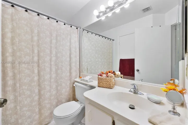 Bathroom featuring an integrated vanity countertop with an oval basin, a large wall-mounted mirror, and multi-bulb Hollywood-style light fixture