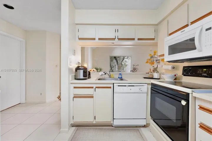 Kitchen featuring white cabinetry, integrated microwave, stainless steel sink, tile flooring, and a passthrough opening