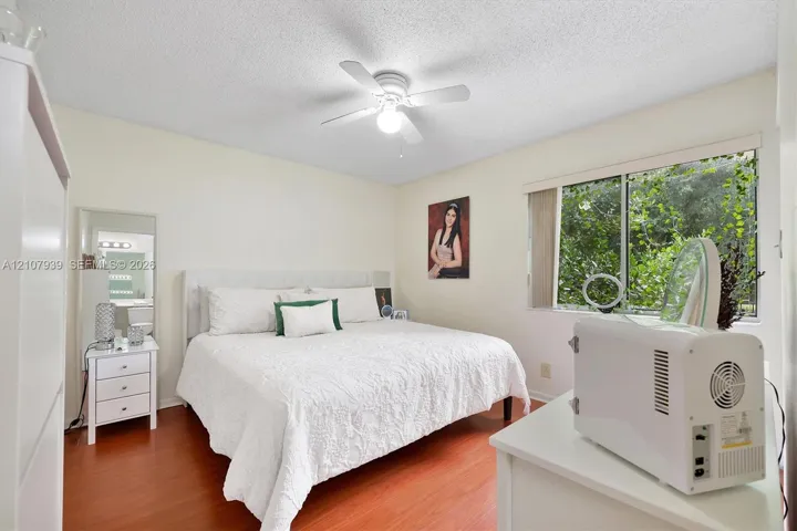 Bedroom featuring wood-finish flooring, a ceiling fan with integrated lighting, and a window with neutral-toned blinds