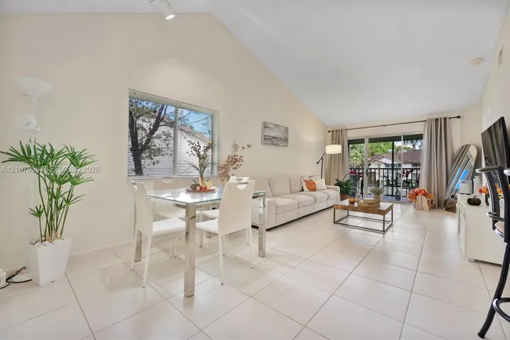 Vaulted ceilings, large-format tile flooring, oversized window, and sliding glass door leading to a private balcony