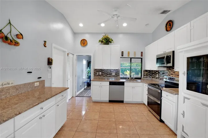 Kitchen featuring white cabinetry, stone-surface countertops, tile flooring, stainless steel appliances, and multi-tone decorative tile backsplash