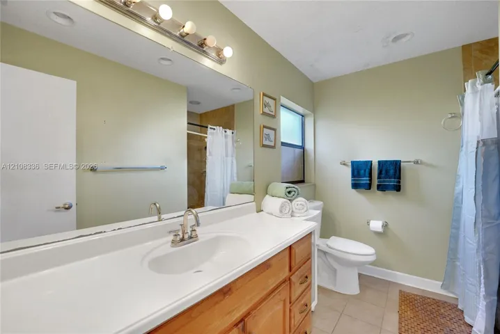 Bathroom featuring a wood vanity with an integrated countertop sink, wall-spanning mirror, multi-bulb vanity light, and tiled flooring