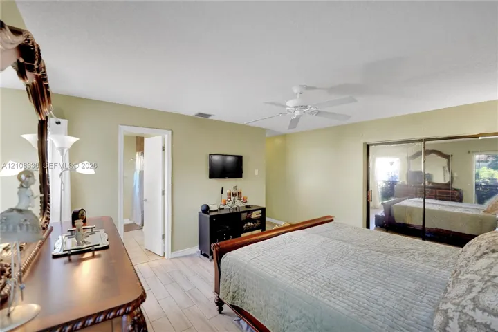 Neutral-toned bedroom featuring wood-finish tile flooring, ceiling fan, and sliding mirrored closet doors