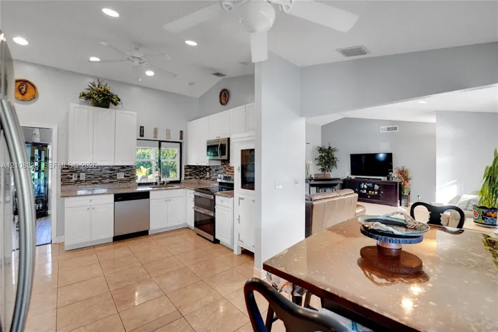 Kitchen featuring white cabinetry, stone-finish countertops, stainless steel appliances, a multi-tone decorative backsplash, and ceramic tile flooring under a vaulted ceiling