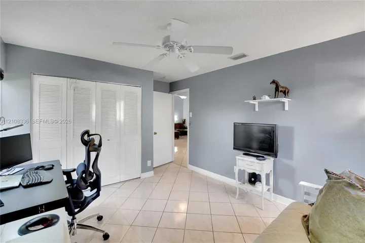 Room featuring neutral-toned walls, tile flooring, louvered bi-fold closet doors, a white ceiling fan, and a wall-mounted display shelf