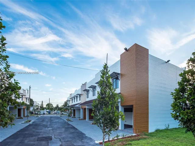 Modern two-story exterior featuring horizontal wood-finish siding, white lap siding, geometric metal window awnings, and an asphalt driveway with paved parking sections