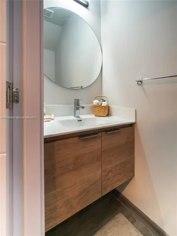 Floating wood-finish vanity with integrated sink, solid surface countertop, chrome single-handle faucet, and oval wall-mounted mirror