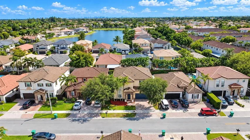 Aerial perspective of suburban residential properties featuring paver driveways, two-story architectural designs, pitched tile roofs, and manicured landscaping