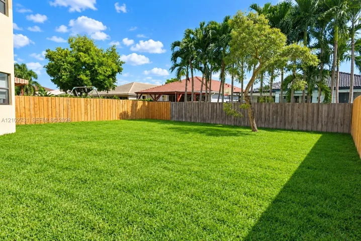 Expansive backyard featuring a level lawn, natural wood perimeter fencing, and mature palm trees