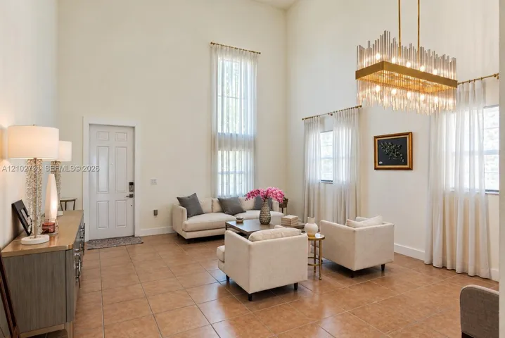 High ceilings featuring an expansive floor-to-ceiling window, tile flooring, and a large multi-tiered rectangular chandelier with crystal accents