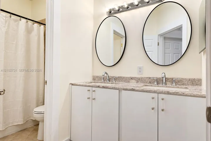 Dual-sink vanity featuring stone-composite countertops, undermount sinks, polished chrome fixtures, dual oval mirrors with black frames, and modern cabinet hardware