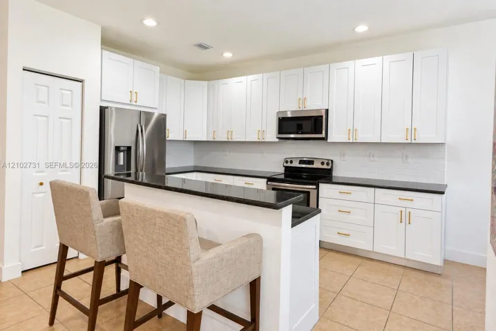 Kitchen featuring white shaker-style cabinetry, dark stone countertops, stainless steel appliances, a breakfast bar, and tile flooring