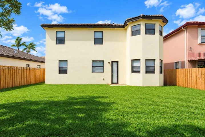 Two-story exterior featuring a stucco facade, multi-faceted architectural bay, tile roof, and enclosed fenced backyard with lawn