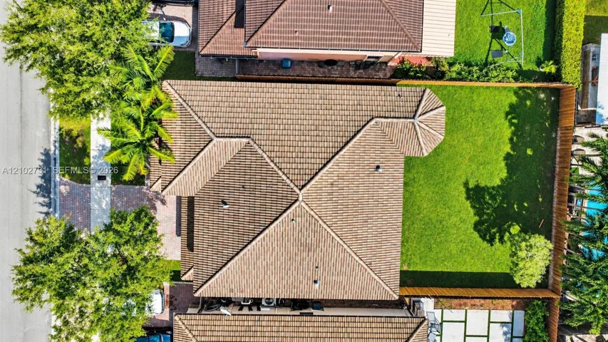 Aerial perspective featuring a hip roof, paved front walkway, fenced backyard, and mature landscaping