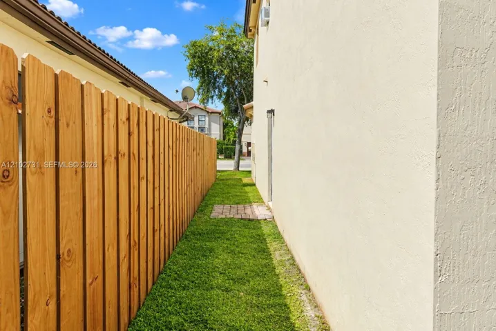 Side yard featuring a natural wood privacy fence, stucco exterior finish, and a brick paver pathway