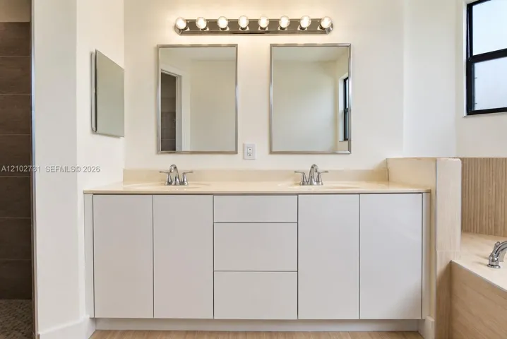 Dual-sink vanity with clean-lined cabinetry, solid-surface countertop, dual metal-framed mirrors, and eight-bulb fixture