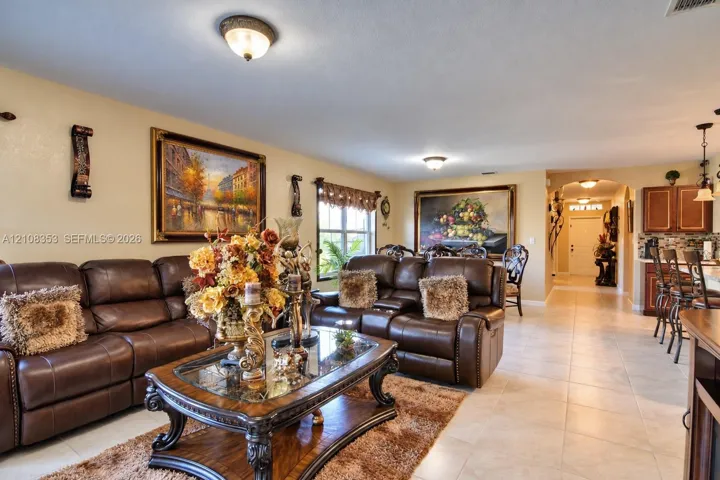 Open-concept interior featuring neutral tile flooring, recessed and flush-mount lighting, arched architectural detailing, and wood-finish cabinetry
