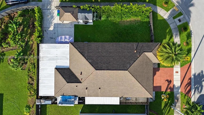 Aerial perspective featuring a multi-pitched composition shingle roof, a paved brick-style walkway, a concrete driveway, and fenced perimeter landscaping