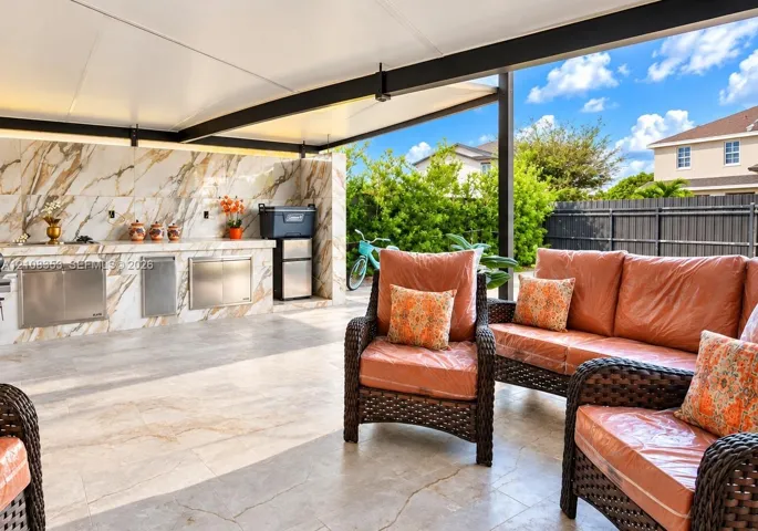 Covered outdoor patio featuring large-format tile flooring, a stone-finish backsplash, and integrated stainless steel cabinetry