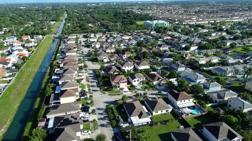 Aerial perspective of residential neighborhood featuring paved streets, managed landscaping, and a bordering canal