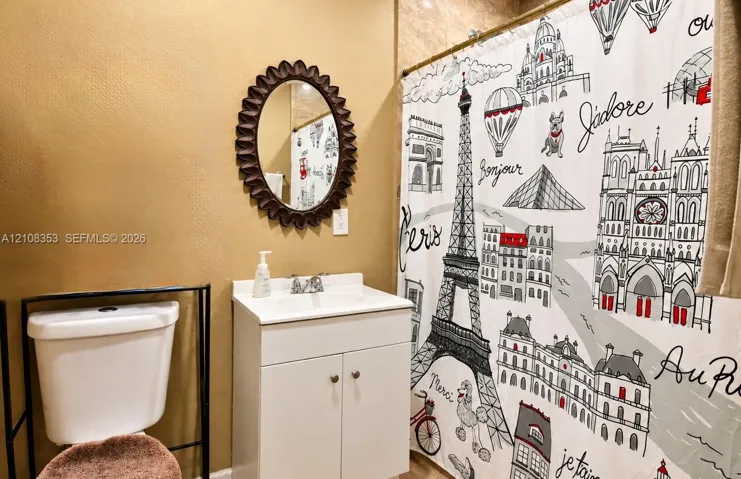 Bathroom featuring a white vanity cabinet with a composite countertop and integrated basin, a scalloped-edge wall mirror, and a ceramic toilet