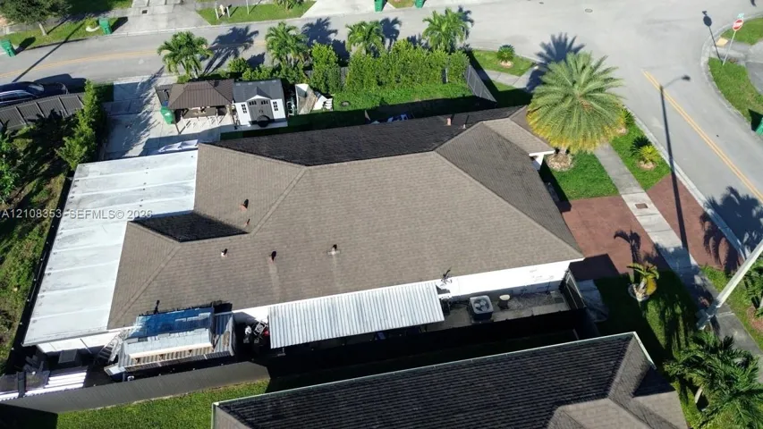 Aerial perspective of a corner lot property featuring a multi-faceted shingle roof, a paved driveway, and an expansive covered outdoor patio area