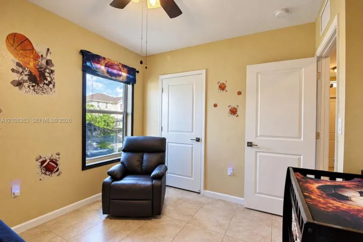 Neutral-toned room featuring tile flooring, multi-panel interior doors, a ceiling fan with light fixture, and a single-pane window with a black frame